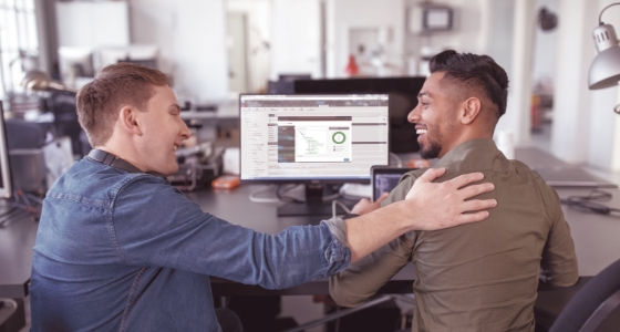 Two colleagues are sitting together in front of a computer, one just sent a web page to translation through a connector; one is patting the other on the back and laughing