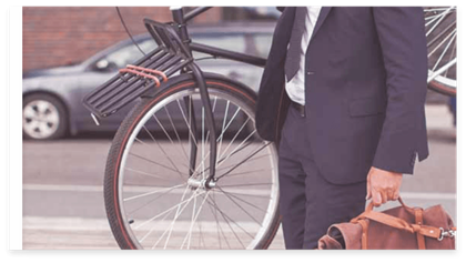 A guy with a suit a suitcase and a bike on his shoulder